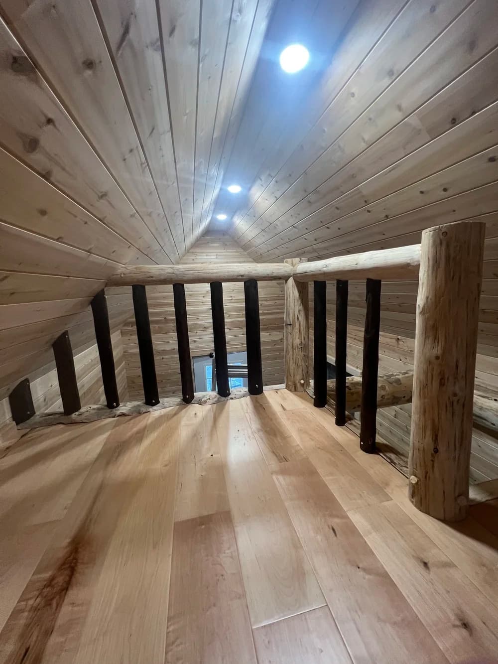 Sleeping loft with wide-plank floors, cedar cathedral ceiling and a log railing