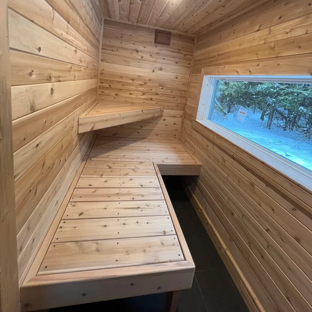 Cedar sauna interior with two-tier benches and a long horizontal window looking onto snowy woods