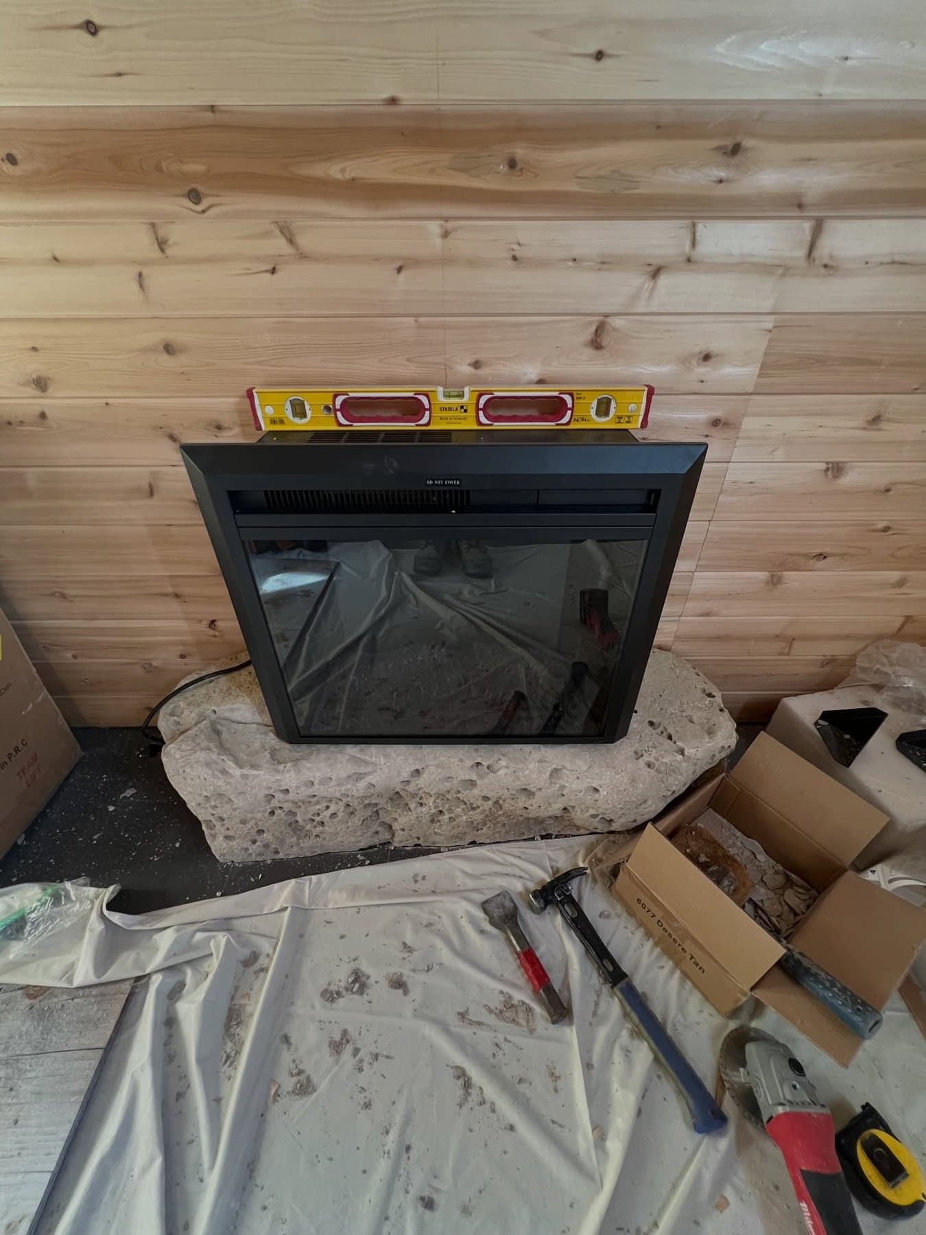 Electric fireplace insert set on a rough fieldstone base against a bare cedar wall, with a level resting on top