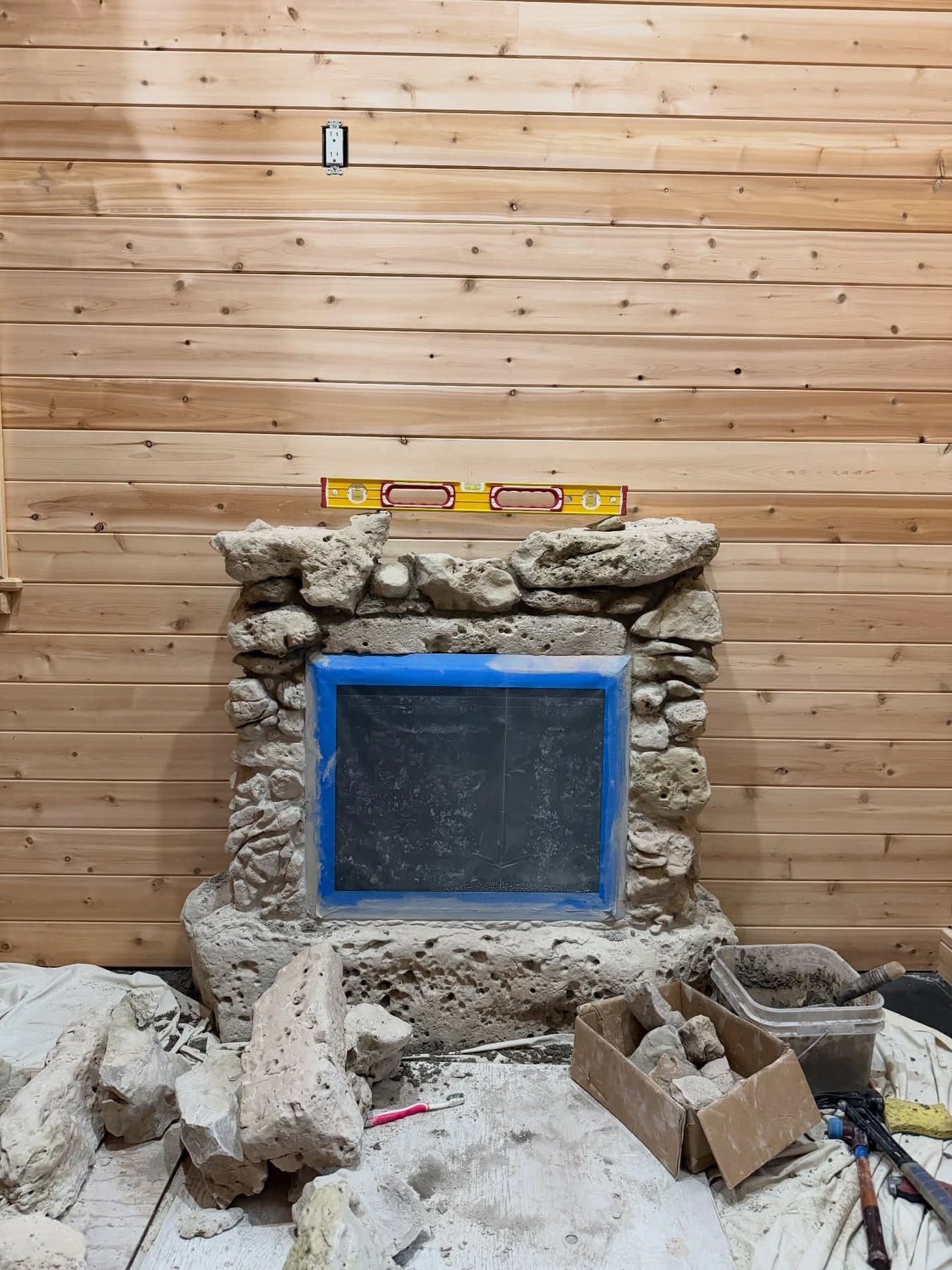 Fieldstone being built up around a taped-off fireplace insert against a cedar wall