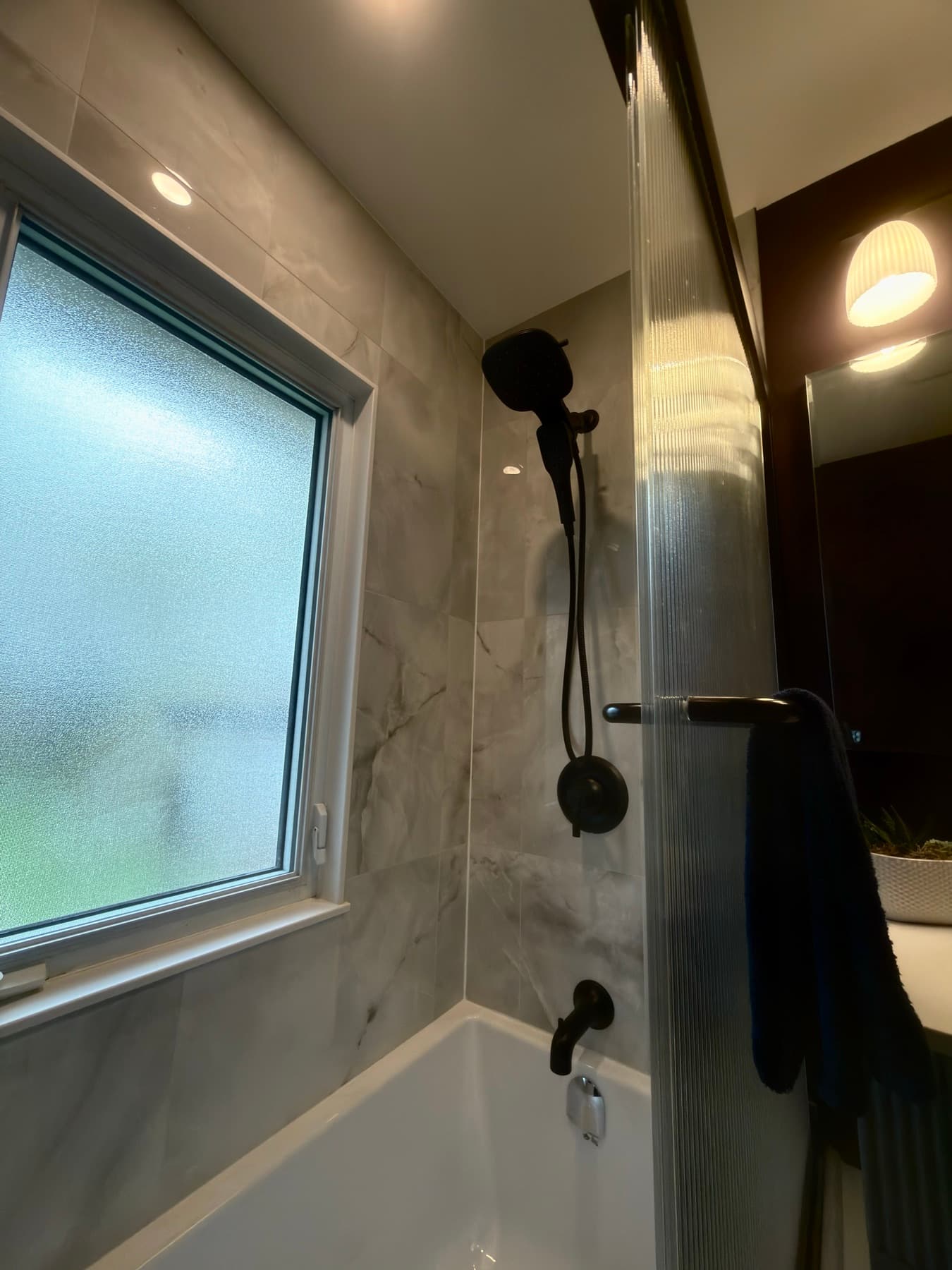 Marble-look tile tub surround with matte black fixtures and a frosted window