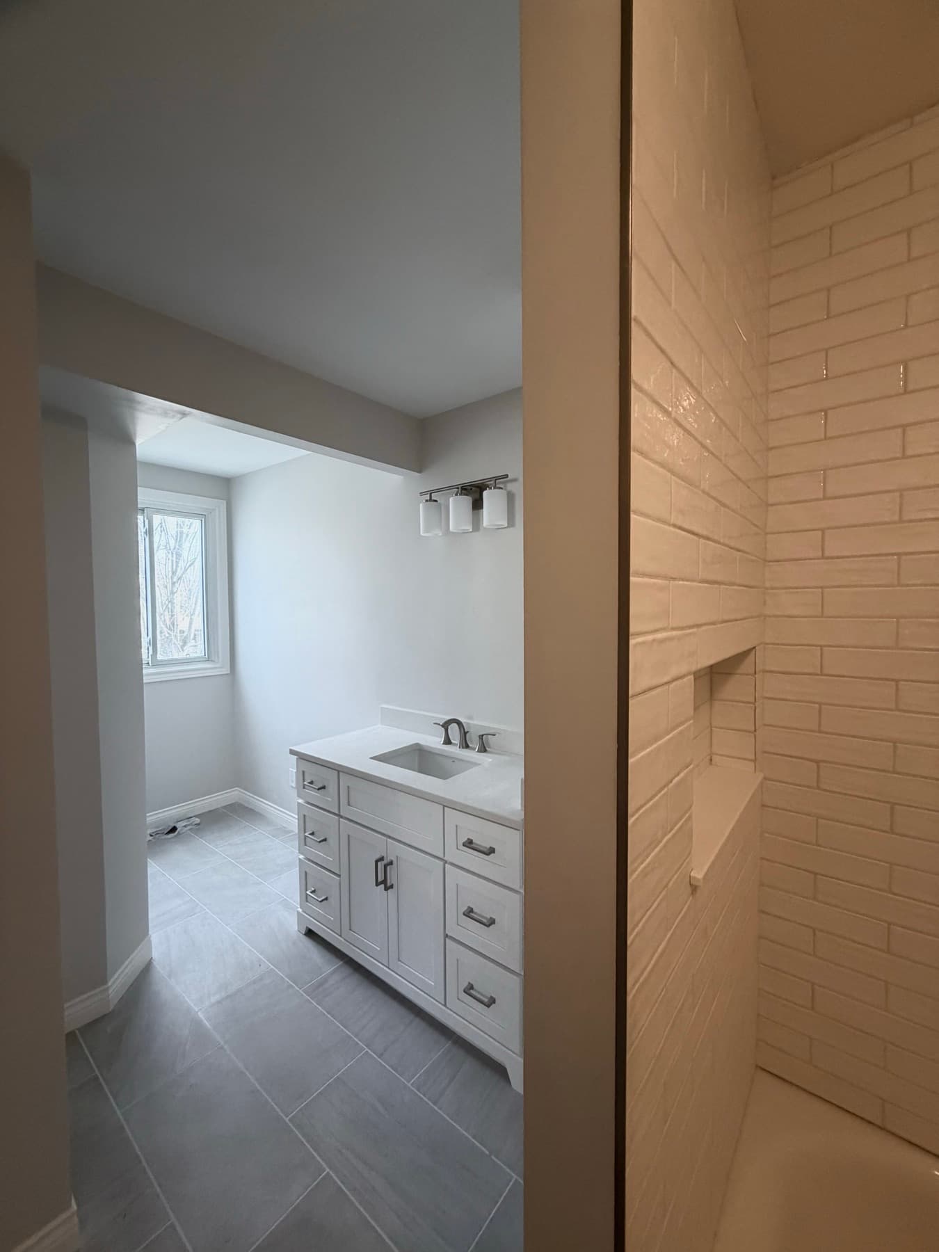 Full-height white subway tile shower surround with a framed, sealed niche, vanity visible through the doorway