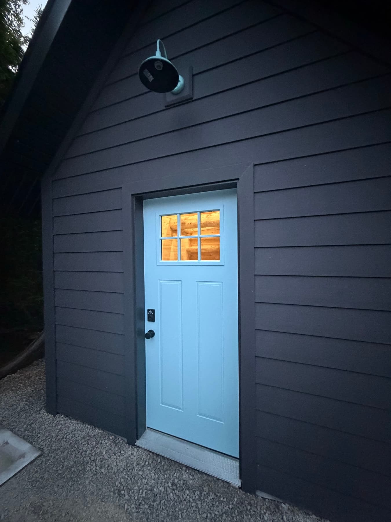 A dark board-and-batten cabin exterior with a light blue door, photographed at dusk