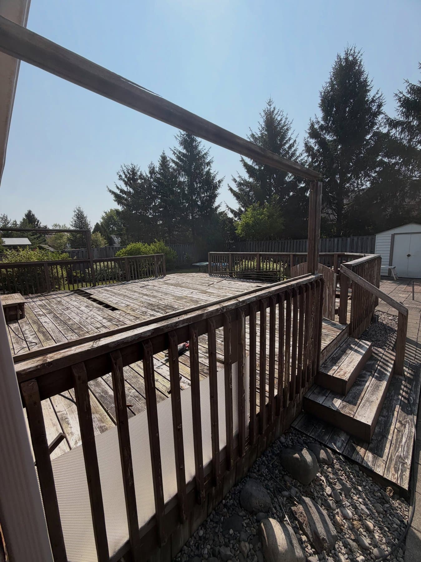 A weathered grey deck mid tear-off, with old railings and splintering boards