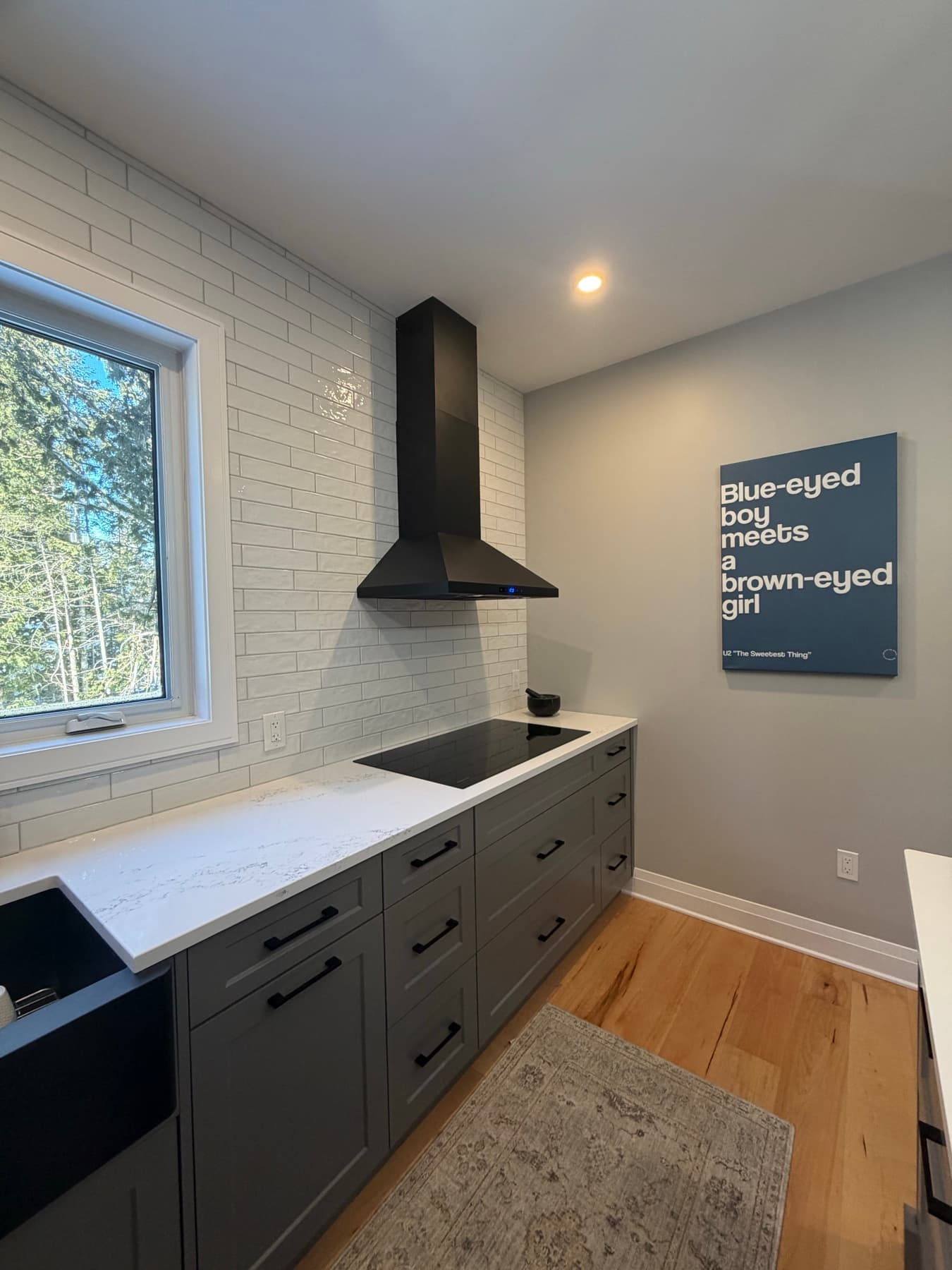 Dark shaker cabinetry with a black chimney hood over an induction cooktop and white subway tile backsplash