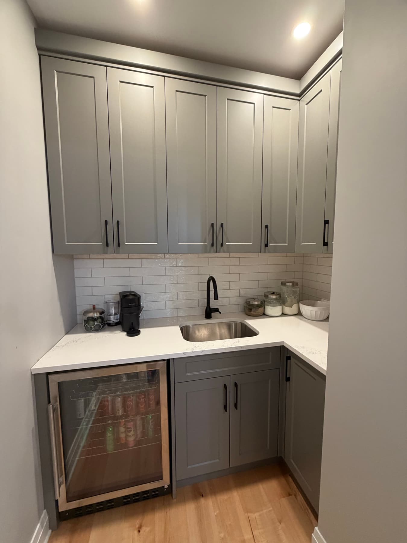 Butler pantry with grey cabinetry, a built-in beverage fridge and a subway-tile backsplash