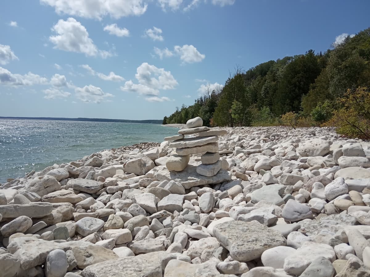 A stone cairn on the white dolomite rock shoreline of Georgian Bay near the Bruce Peninsula, turquoise water and forest behind it
