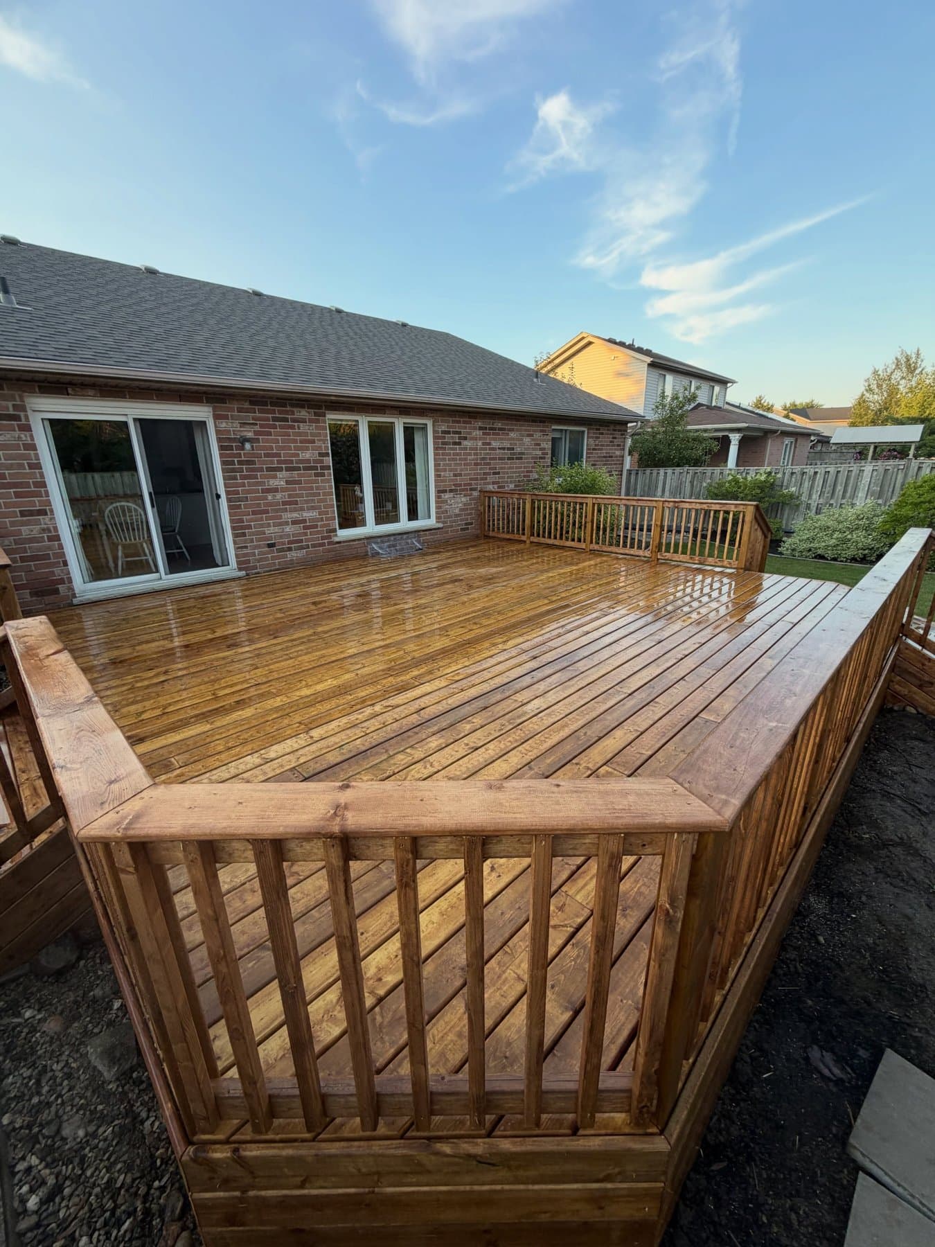 A freshly stained cedar deck in warm evening light against a brick house