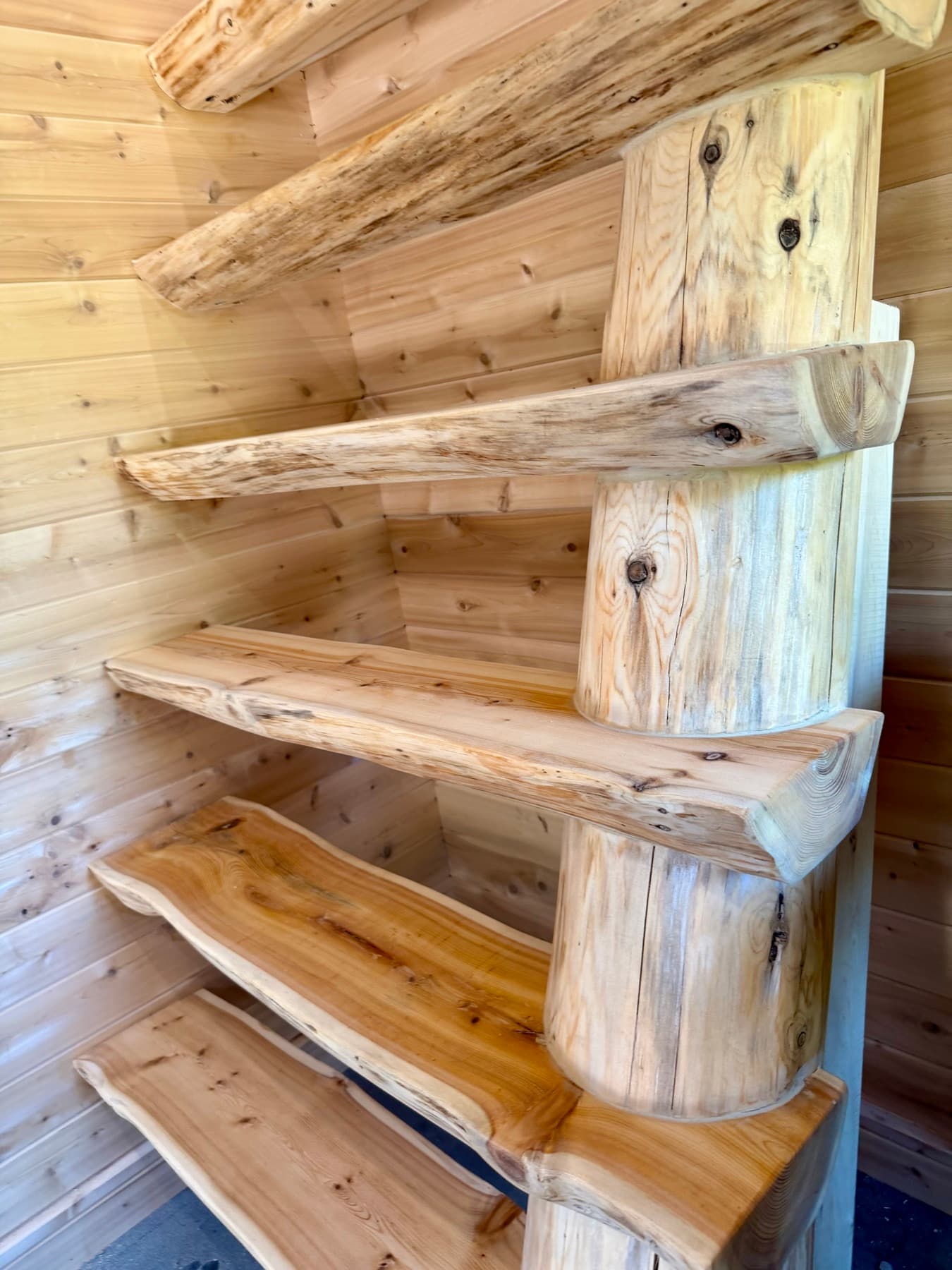 Hand-peeled log stair with treads cantilevered off a single scribed post against a cedar wall